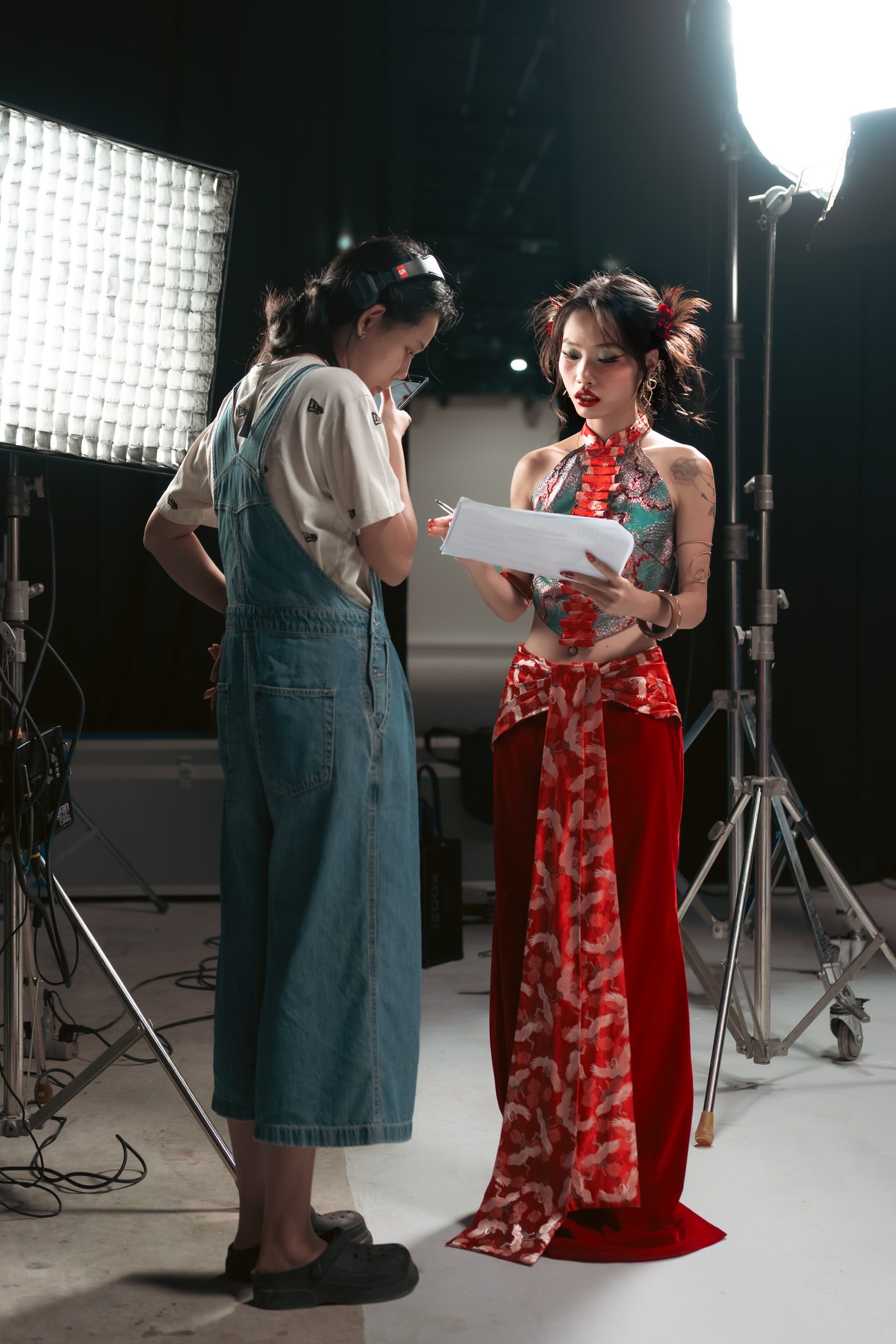 A crew member in denim overalls and an actress in a red and jade costume read the script together